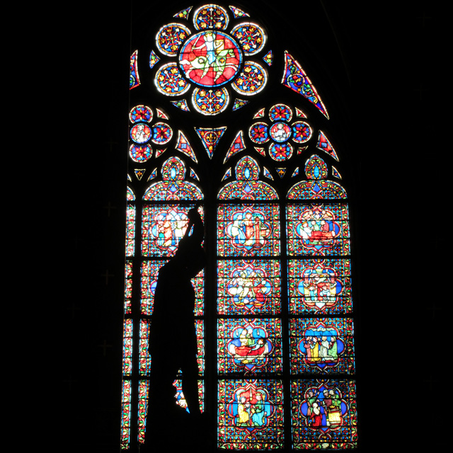 A statue in silhouette in front of a stained glass Notre-Dame window