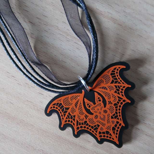 A bat shaped necklace with printed orange lace details by Curiology