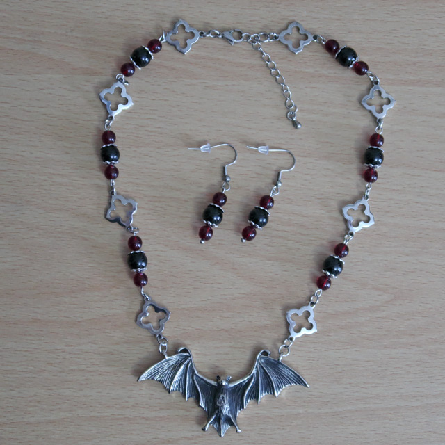 A stainless steel necklace with a bat centrepiece, red glass beads and gothic-style elements